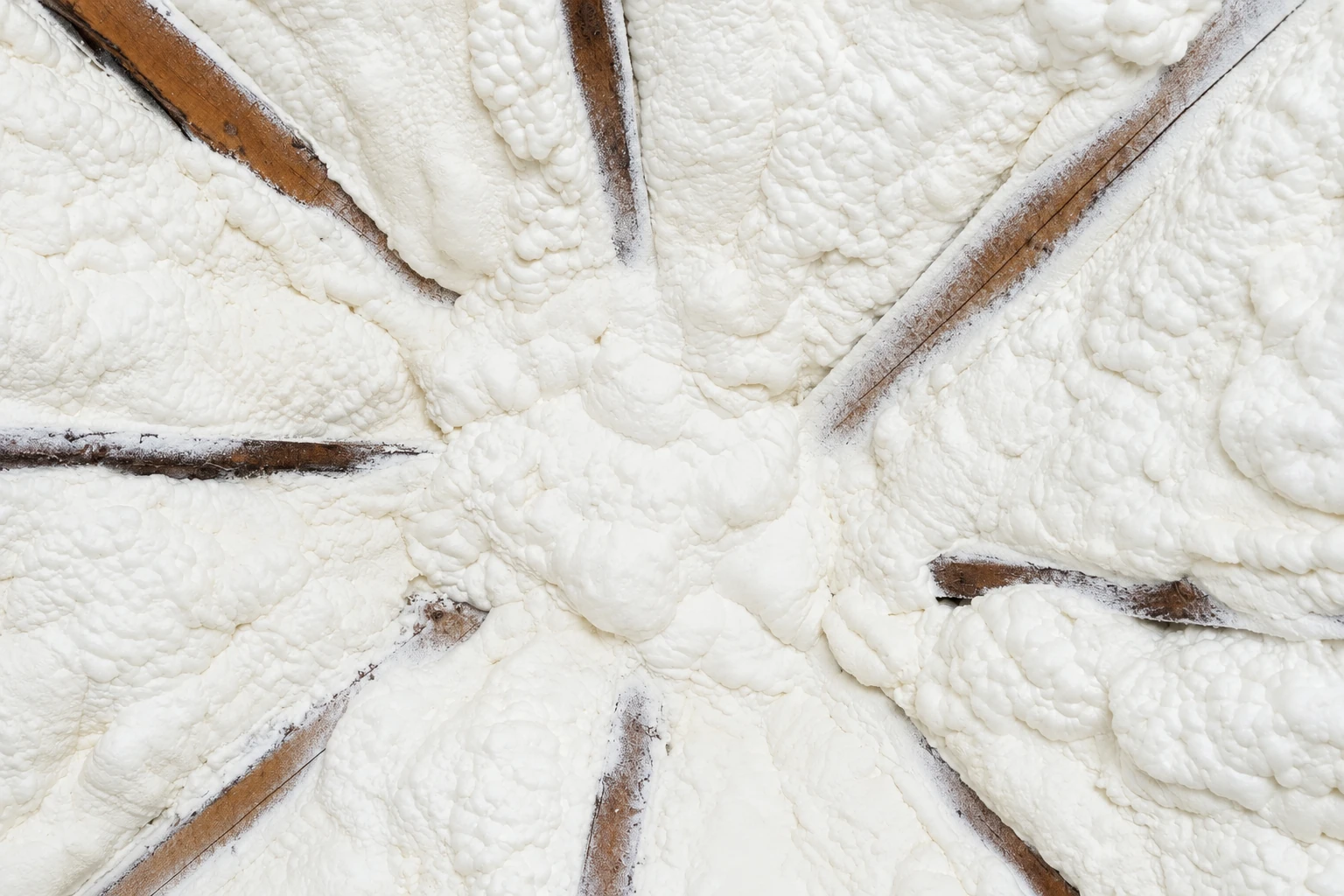 Close-up of thick, uneven white closed-cell spray foam covering exposed wooden framing.