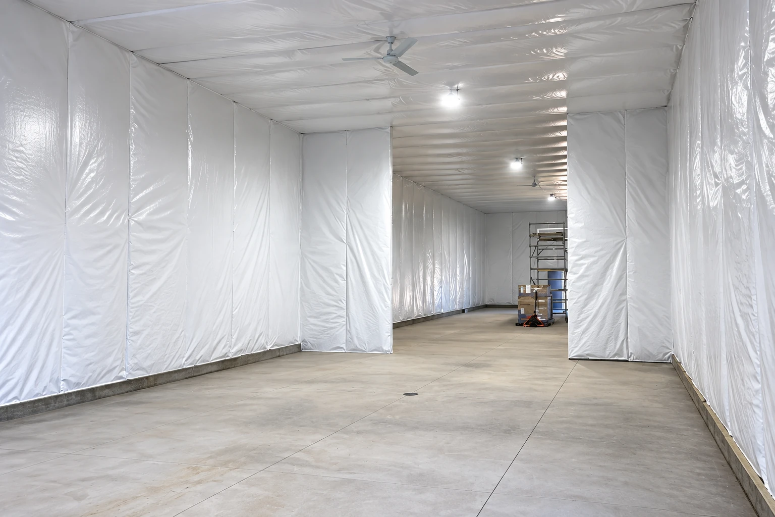 A large commercial room is lined with white plastic sheeting, with a concrete floor and scaffolding in the distance.