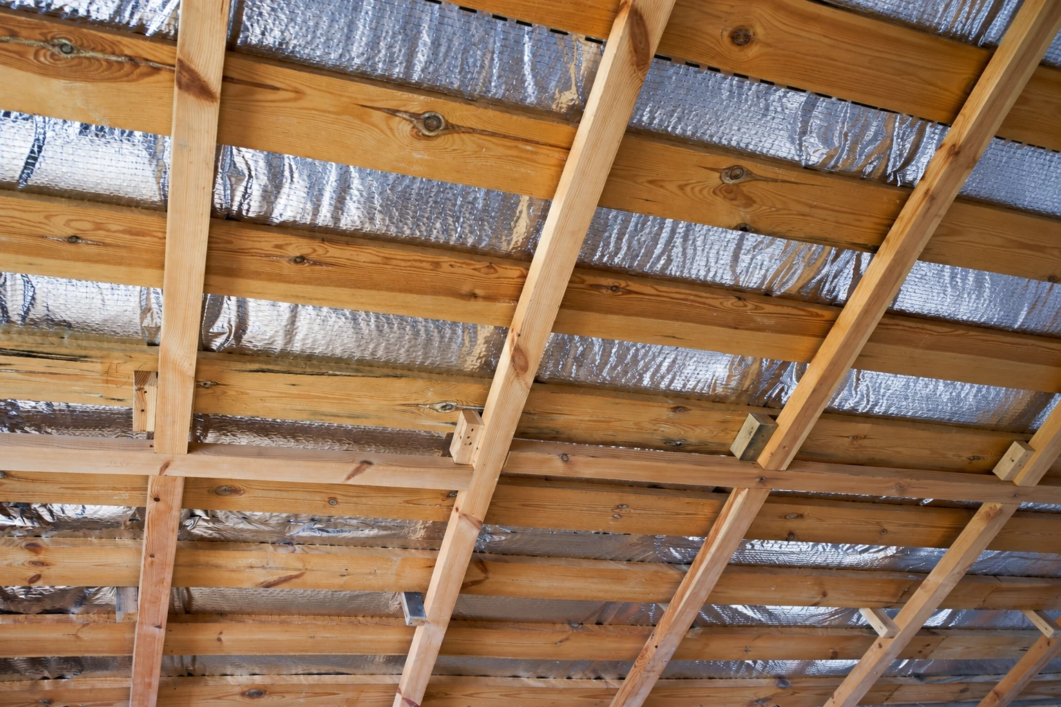 Underside of a wooden roof structure with reflective foil insulation fitted between the rafters.